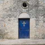 Il portale lunato d�ingresso, che include una porta blu in ferro con croce dorata, � sormontato da un oculo in asse